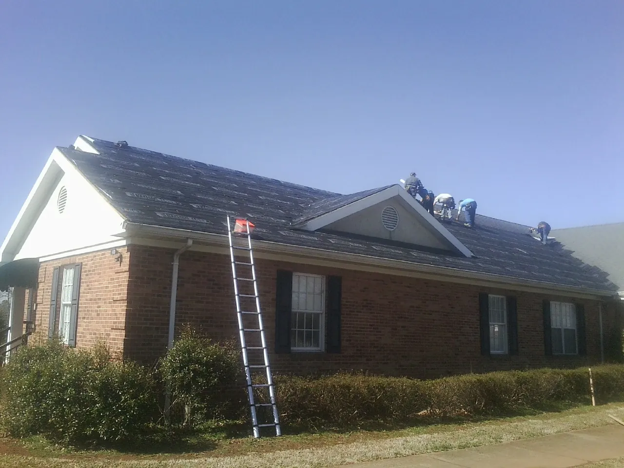 Crew tearing shingles off a brick ranch roof with a ladder set — Metal Roof Repair work by our crew in Havana