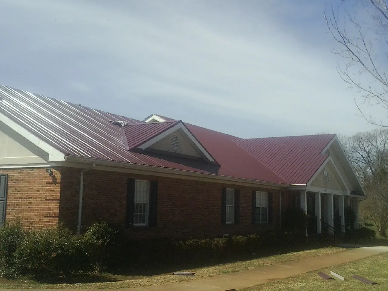 Red metal roof with gabled entries on a long brick building, from a Hail Damage Roof Repair job in Havana