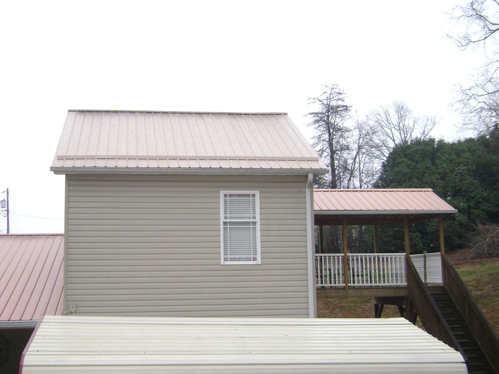 Tan metal roofs on a two story addition and attached porch, from a Roof Replacement job in Havana